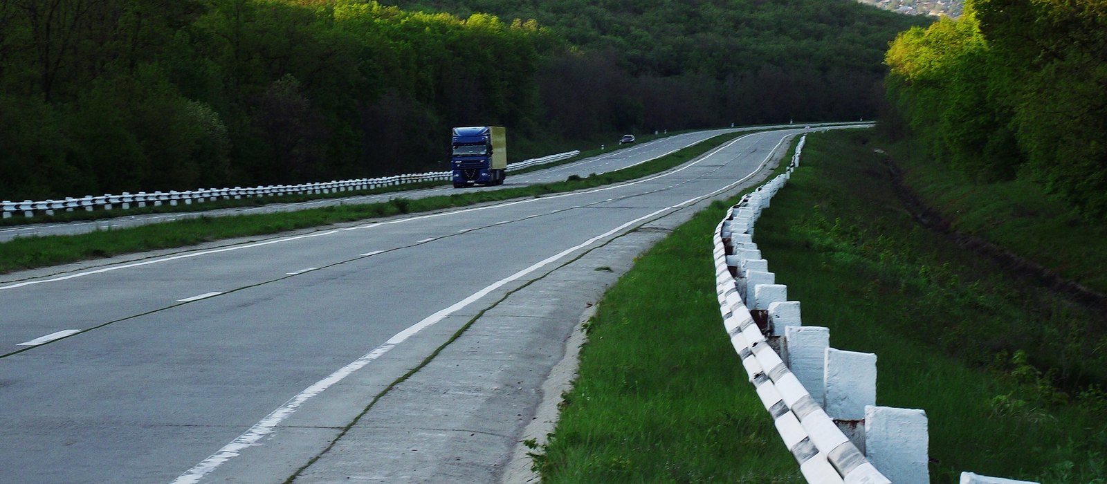 Un camion albastru pe drumul M3 din Republica Moldova, între dealuri împădurite, cu parapet din stâlpi albi pe margine