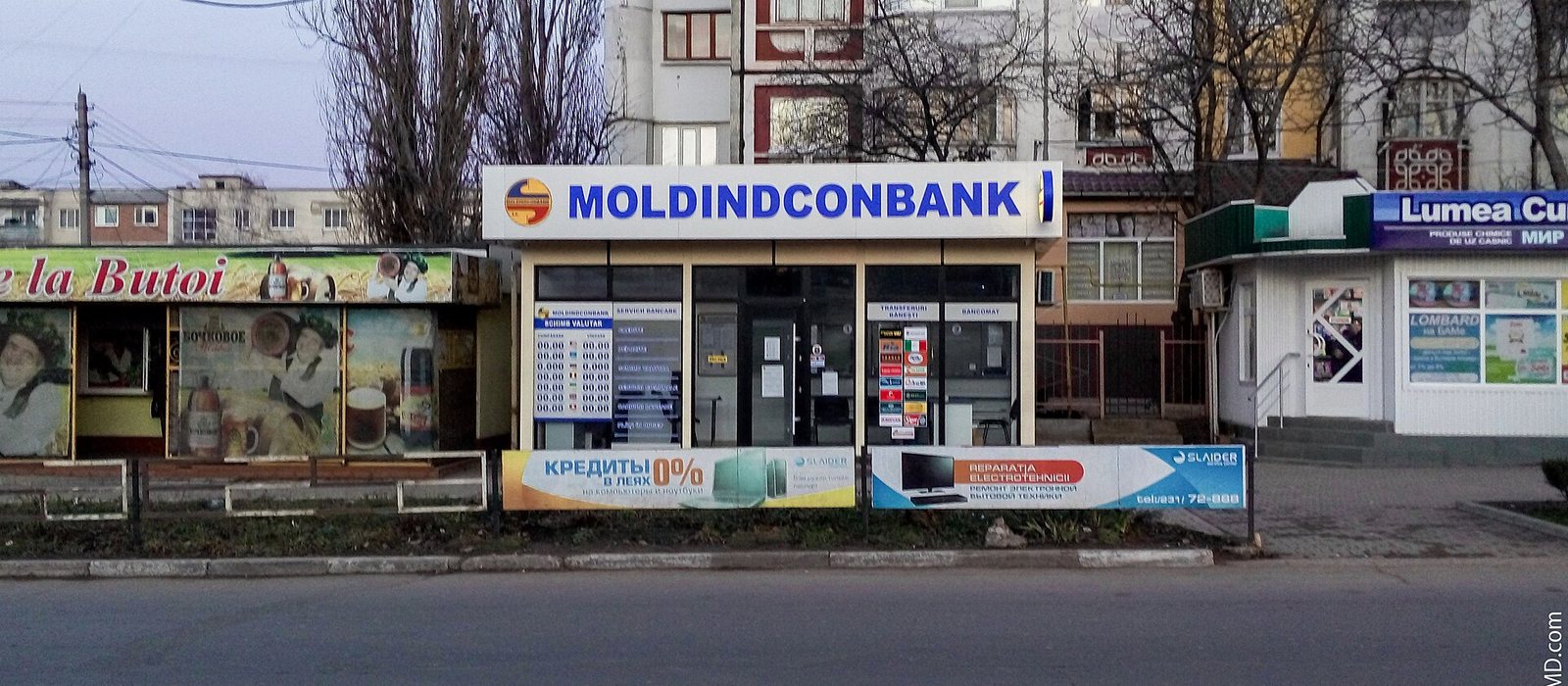 Ghișeu stradal al unei filiale Moldindconbank din Bălți, cu panoul de cursuri valutare în vitrină și blocuri în spate